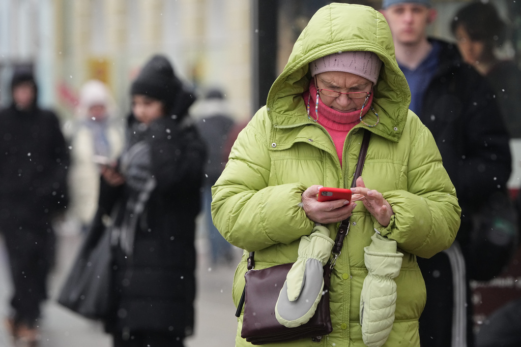 A woman looks at her smartphone at a bus stop in St. Petersburg, Russia, Wednesday, Feb. 11, 2026. (AP Photo/Dmitri Lovetsky)